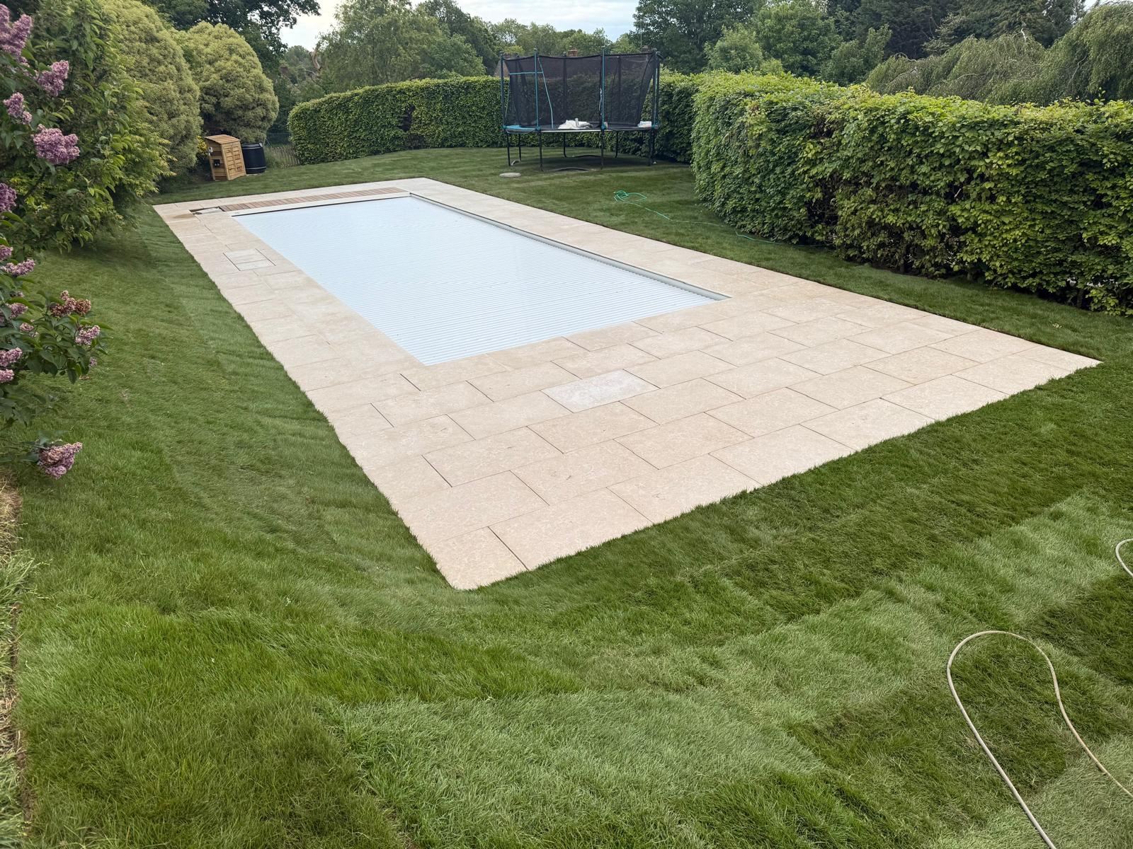 The finished swimming pool with stone surround, automatic cover and freshly laid turf