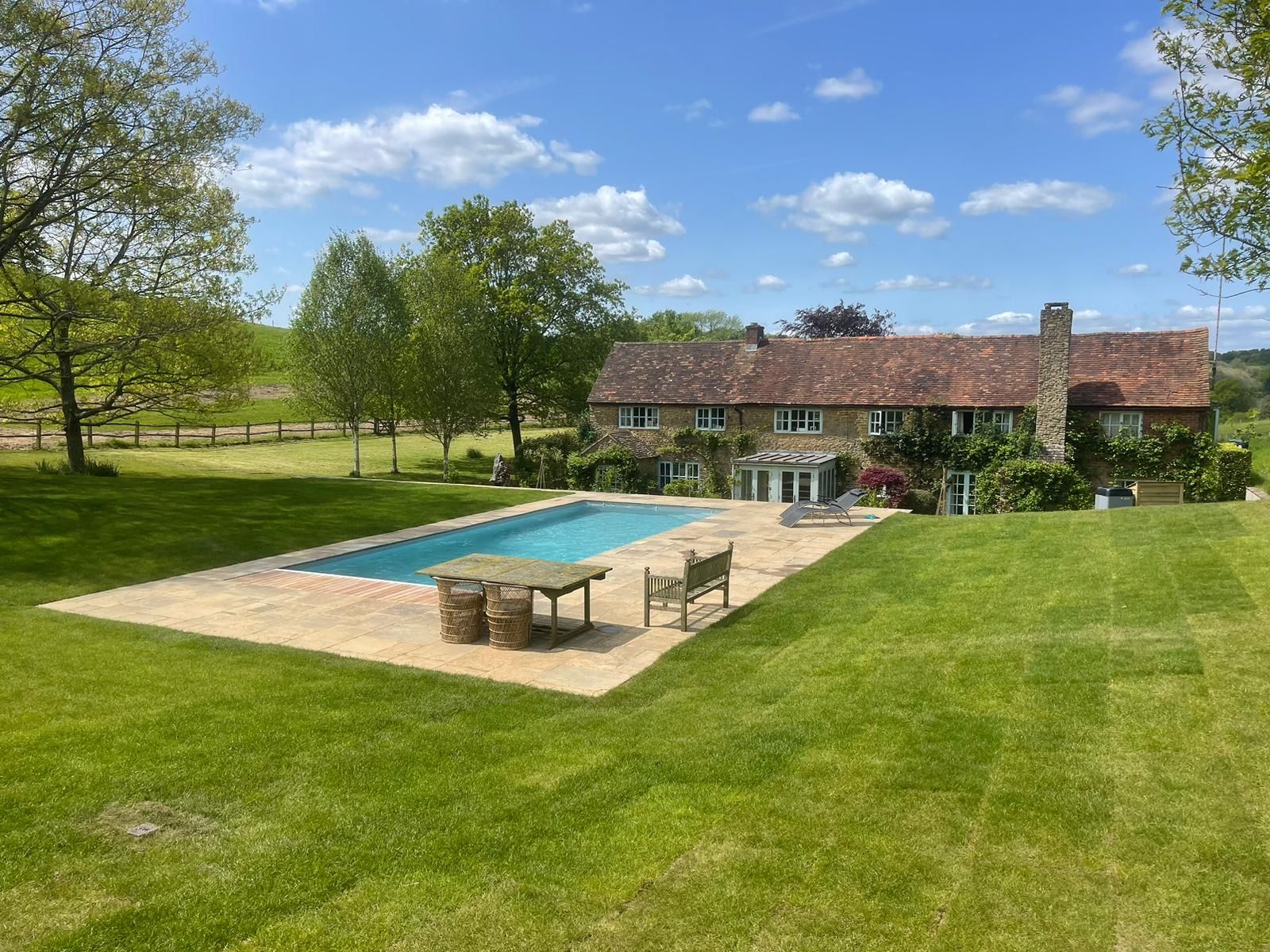 Swimming pool and stone surround set into the lawn of a country farmhouse